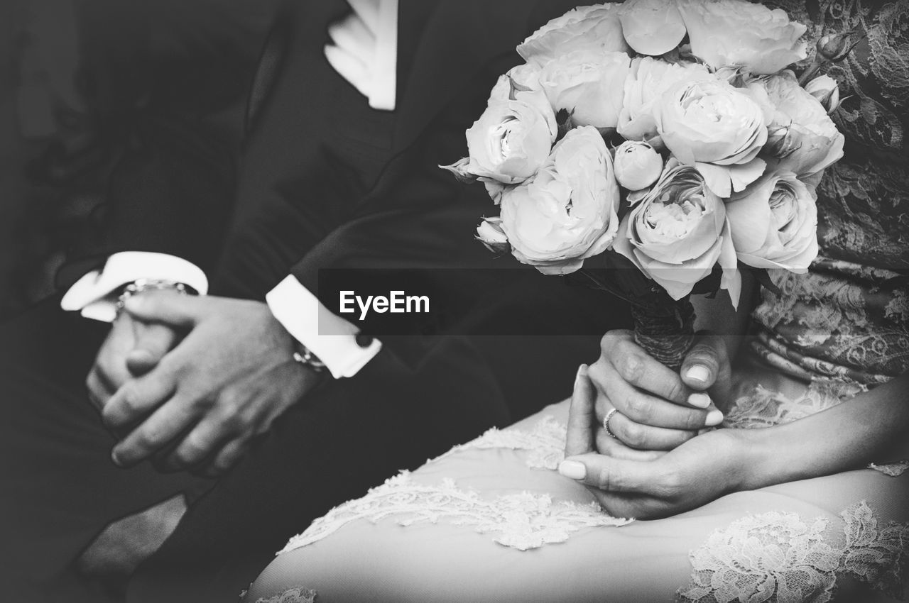 Midsection of bride holding bouquet while sitting by groom