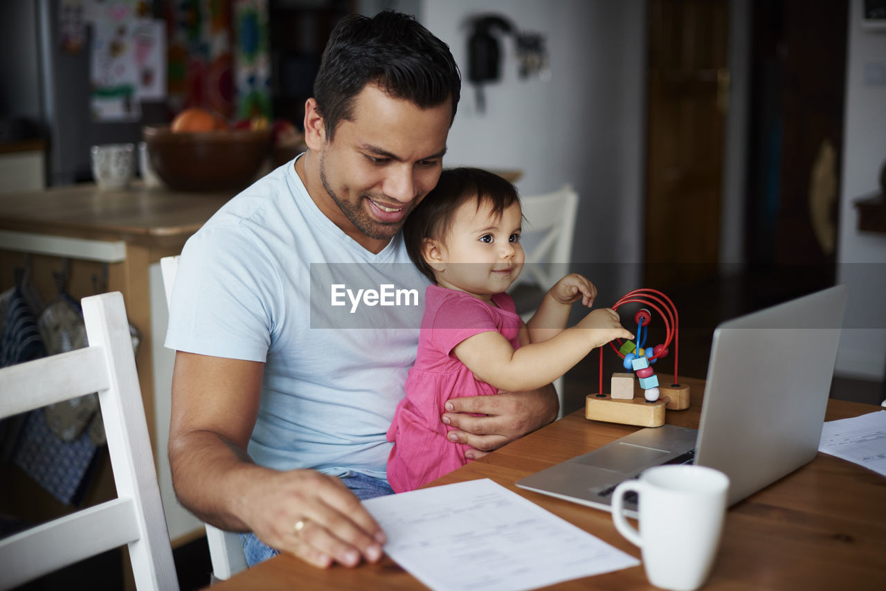 Father with baby girl using laptop on table at home