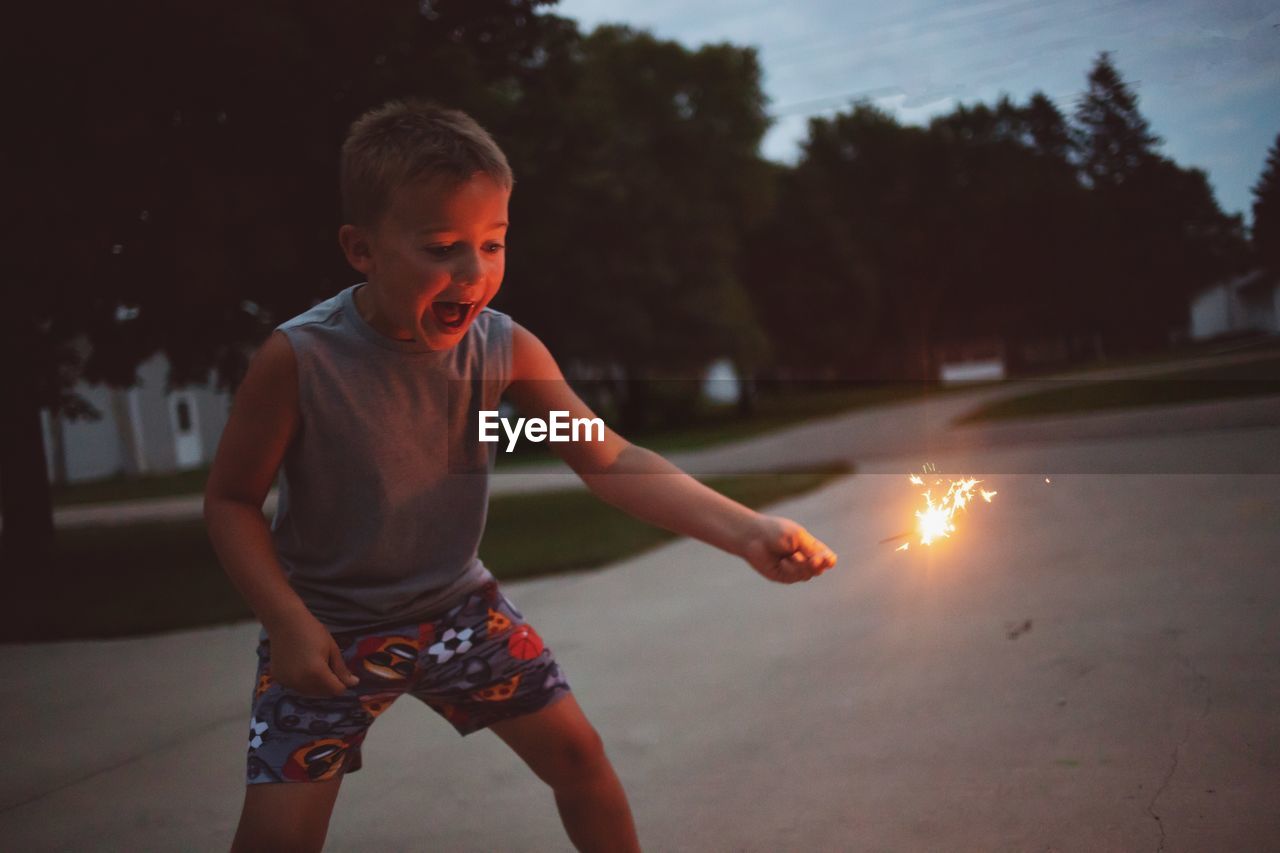 Boy holding sparkler at park during dusk