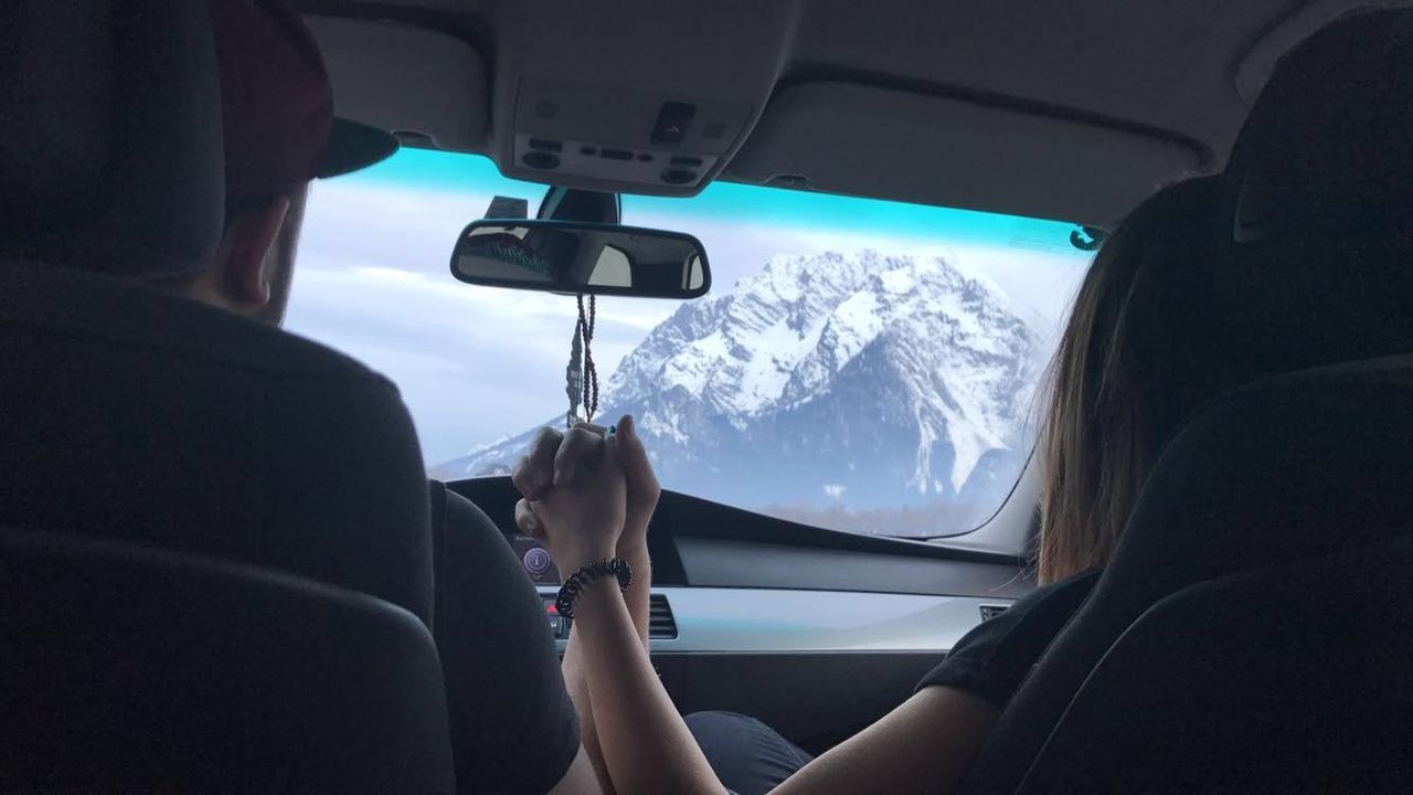 Rear view of couple holding hands while driving car against snowcapped mountain