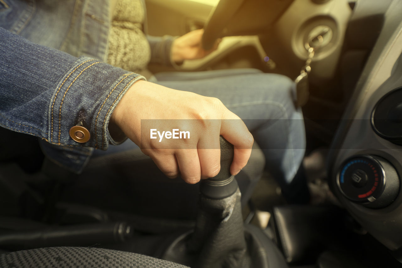 Close up of the hand of a woman on the gear lever while driving inside her vehicle with yellow light