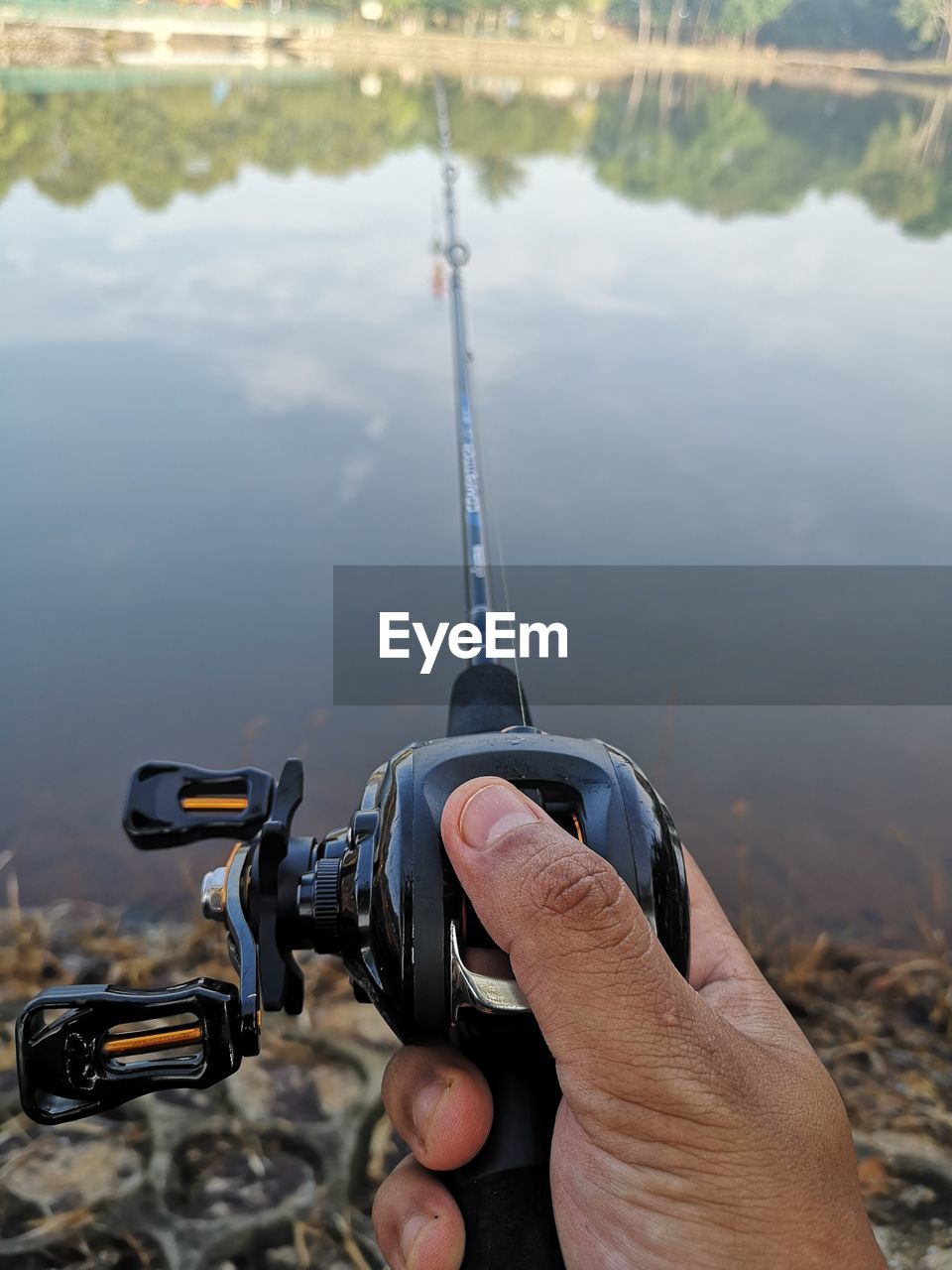 Cropped hand of person holding fishing rod by lake