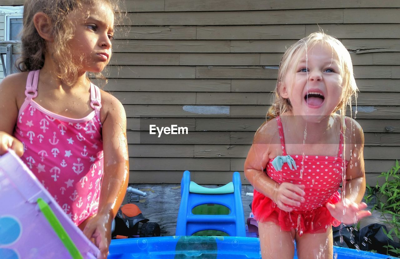 Angry girl throwing water on happy sister