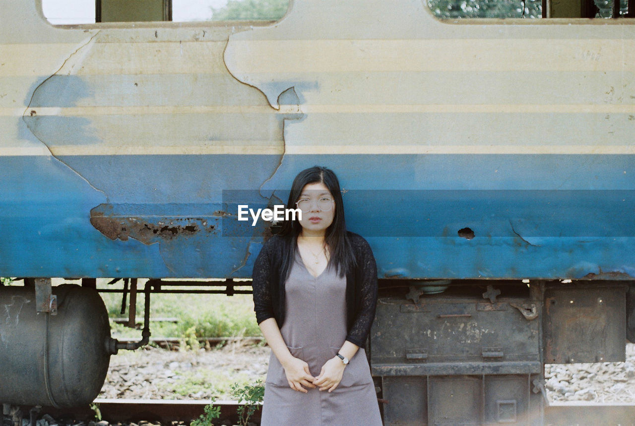 Portrait of young woman standing against abandoned train on railroad track