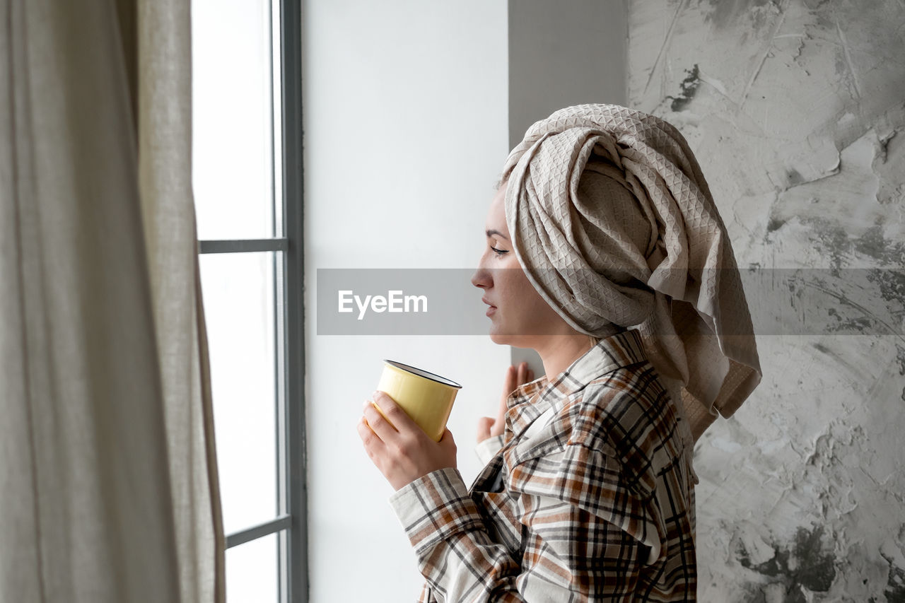 Young woman with towel on her head drinking coffee