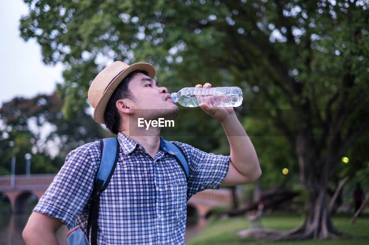 Man drinking water from bottle against tree