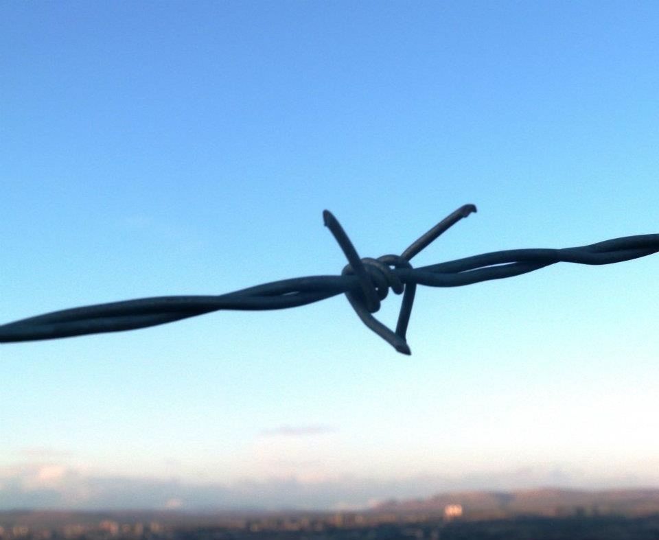 LOW ANGLE VIEW OF BARBED WIRE AGAINST CLEAR BLUE SKY