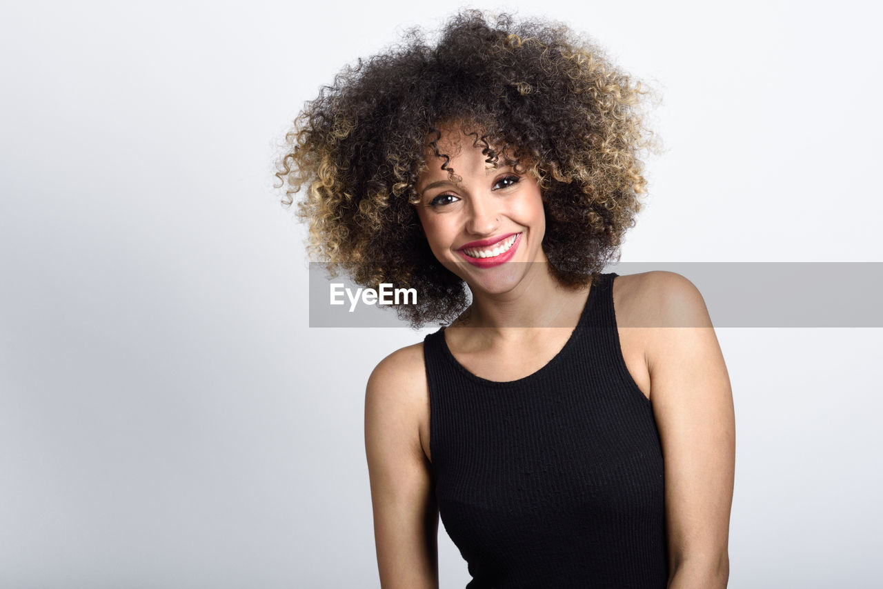 Portrait of smiling young woman with curly hair against white background