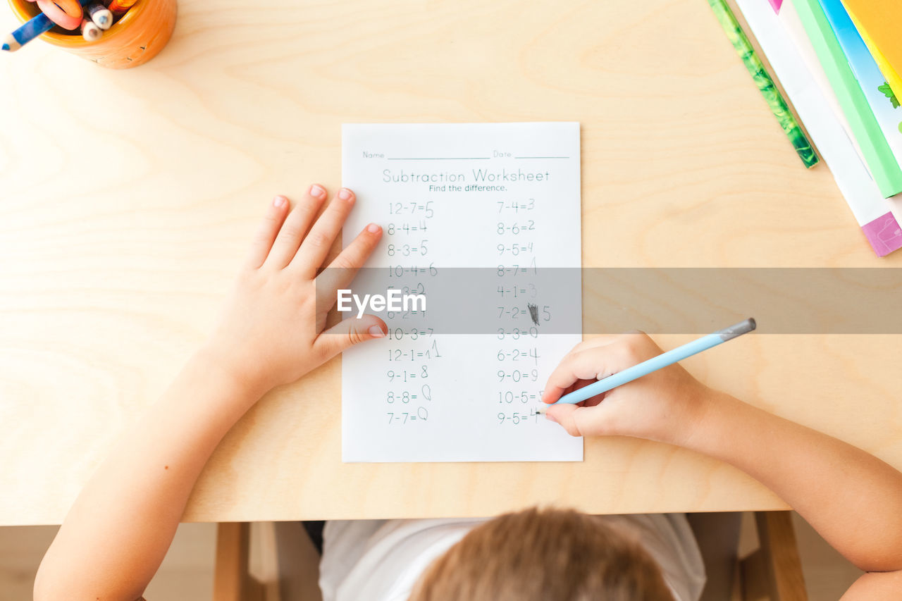 Top view of child hands with pencils. solving maths exercises. 7 years old child doing maths lessons