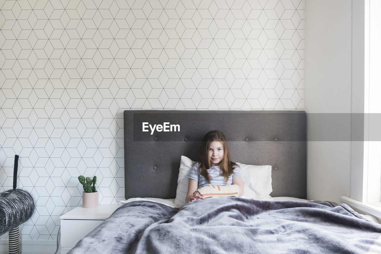 Young girl sitting in bed at home with a broken arm smiling