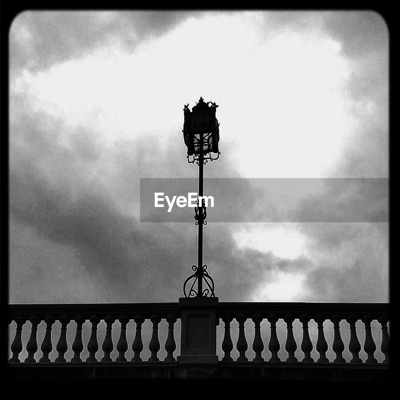 Street light with railing against cloudy sky