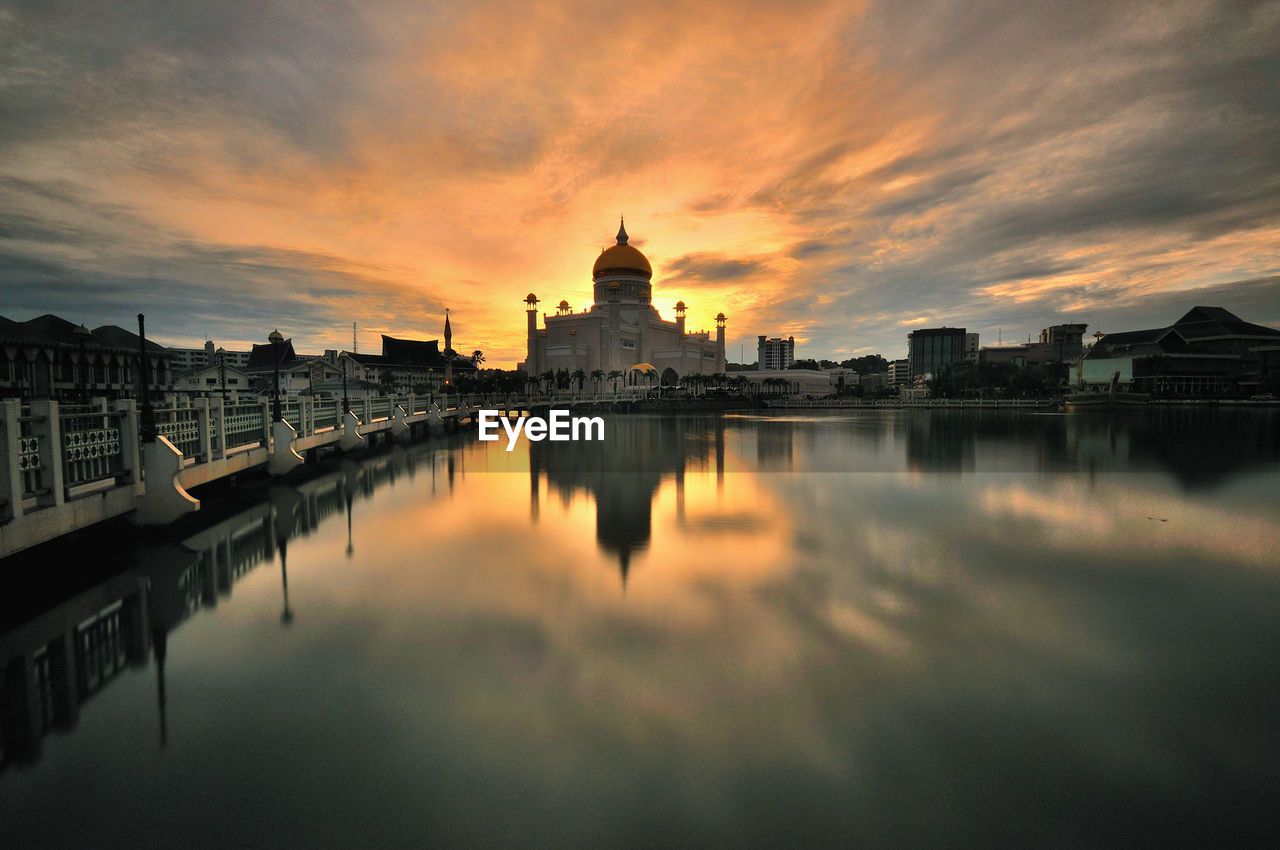 Reflection of mosque in river against sky during sunset