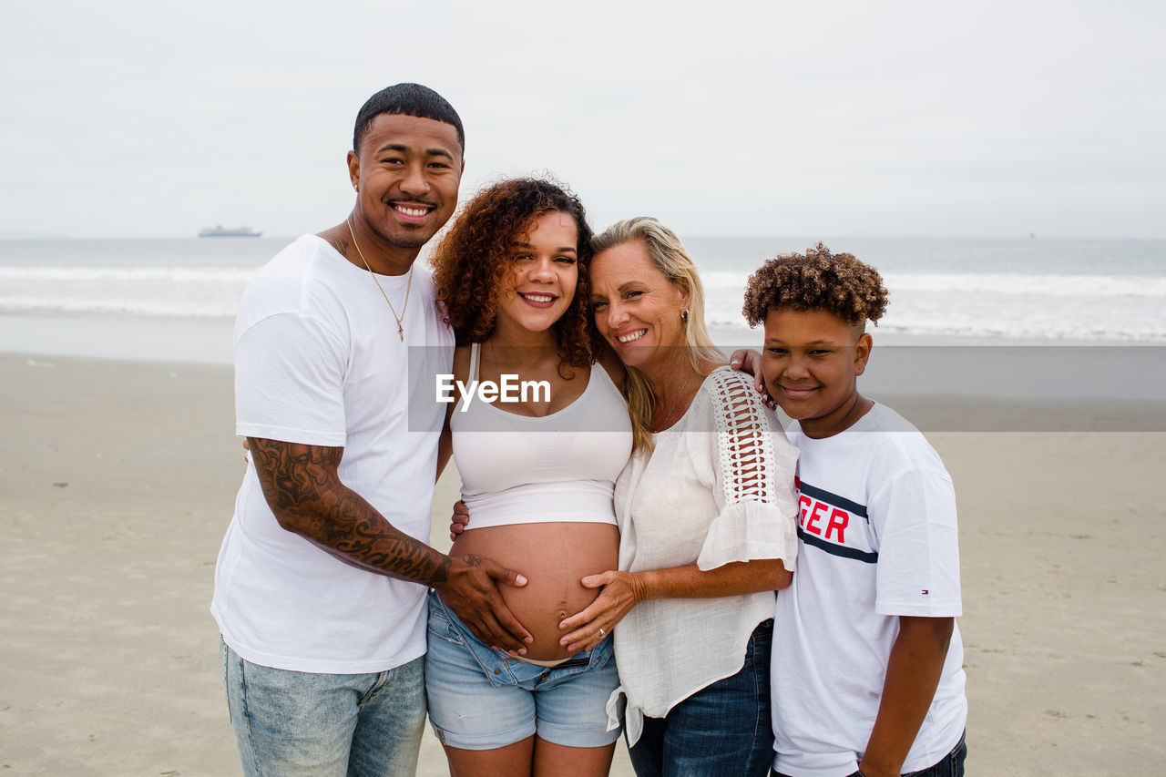 Family posing for maternity photos on beach