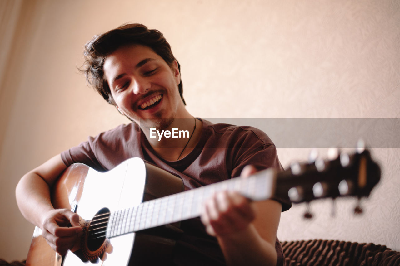 Cheerful young man playing guitar at home