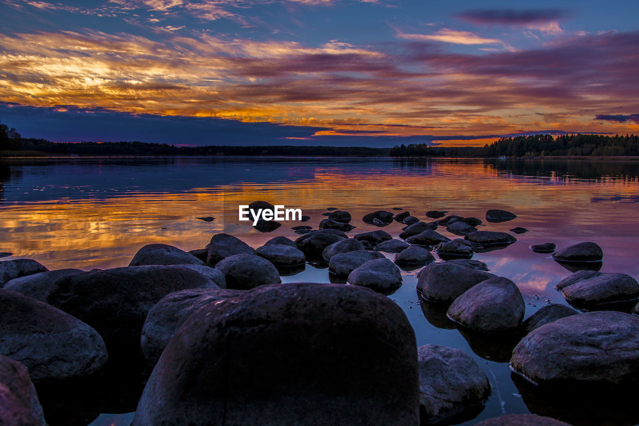 Rocks at shore against sky during sunset