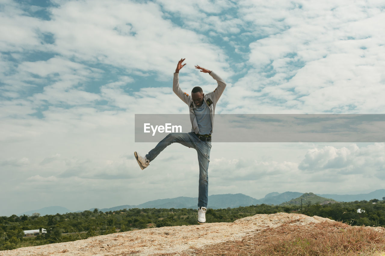 A man jumping on top of a hill against clouds and sky