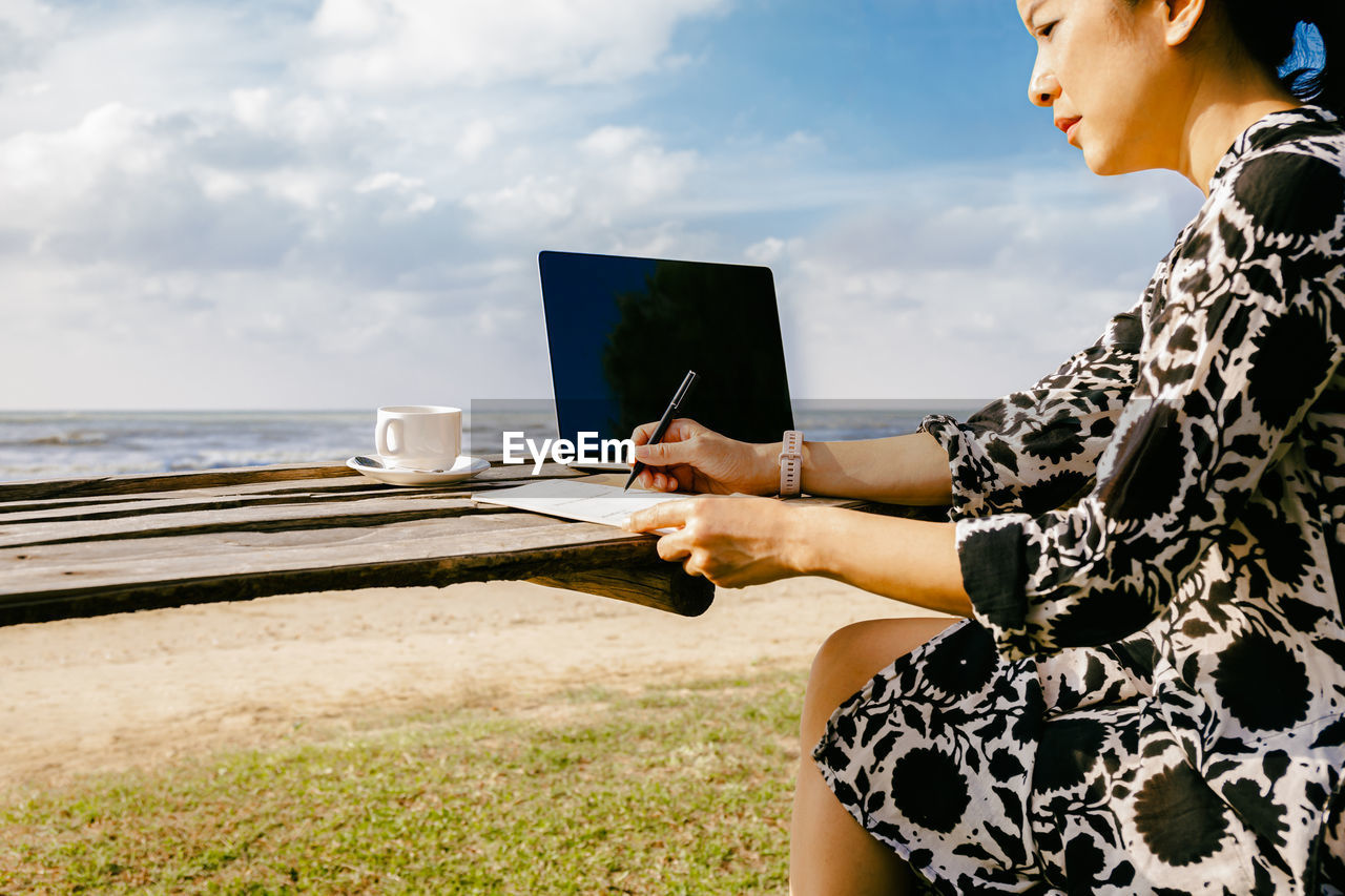 Side view of woman working on laptop computer at beach