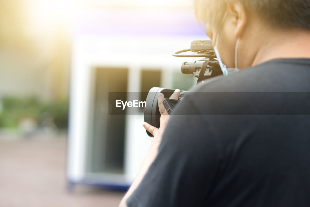 REAR VIEW OF MAN HOLDING CAMERA AT HOME