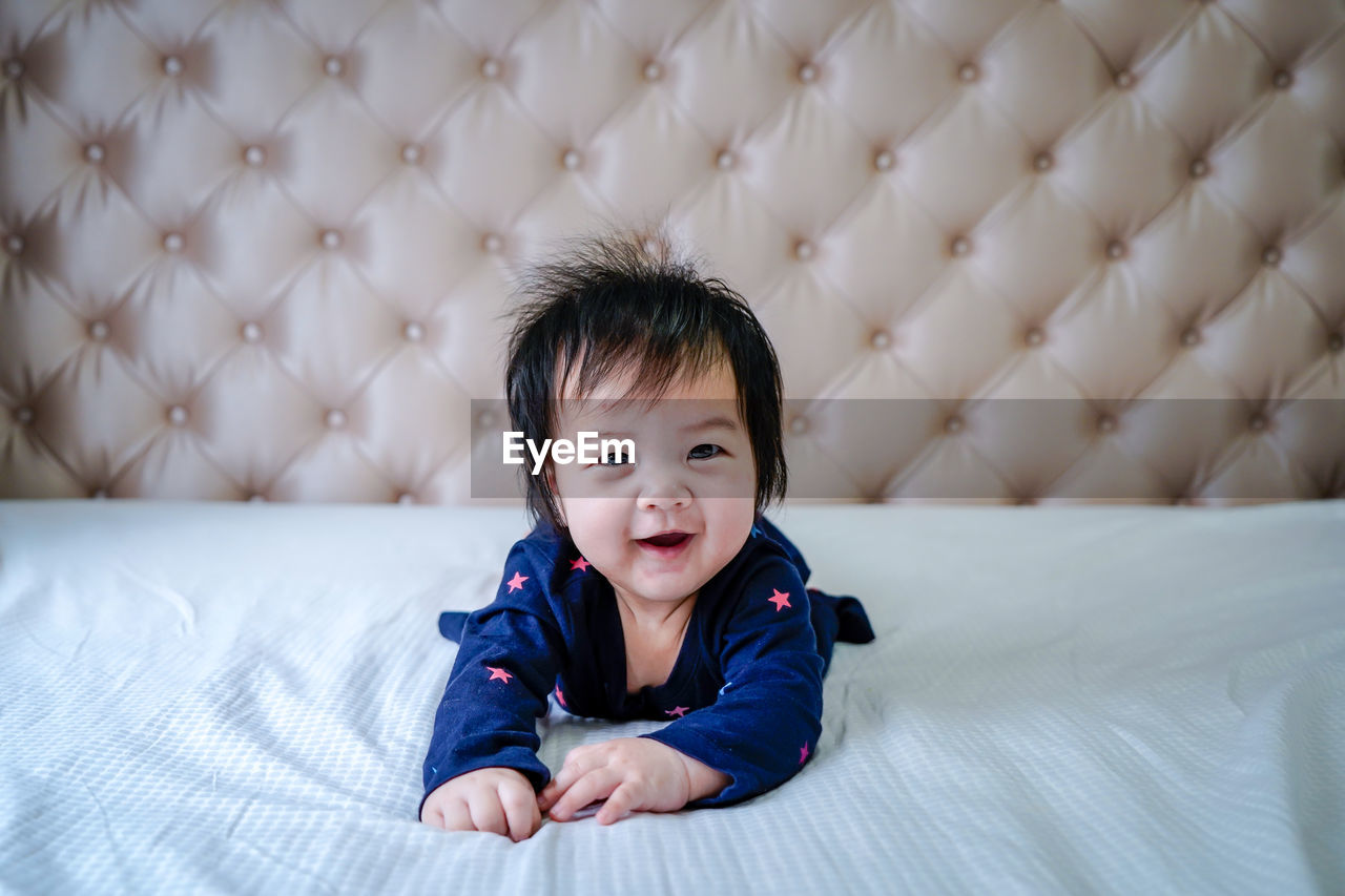 Cute little caucasian baby lying on bed at home. little cute girl in blue dress smiling to camera.