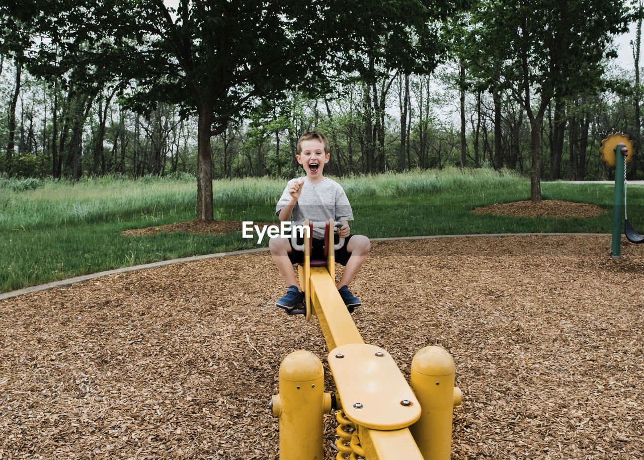 Portrait of happy boy playing on seesaw at park