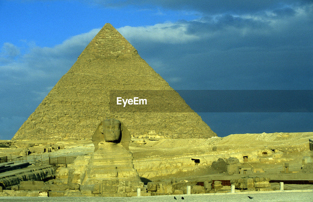 Ancient pyramid and stone statue against sky