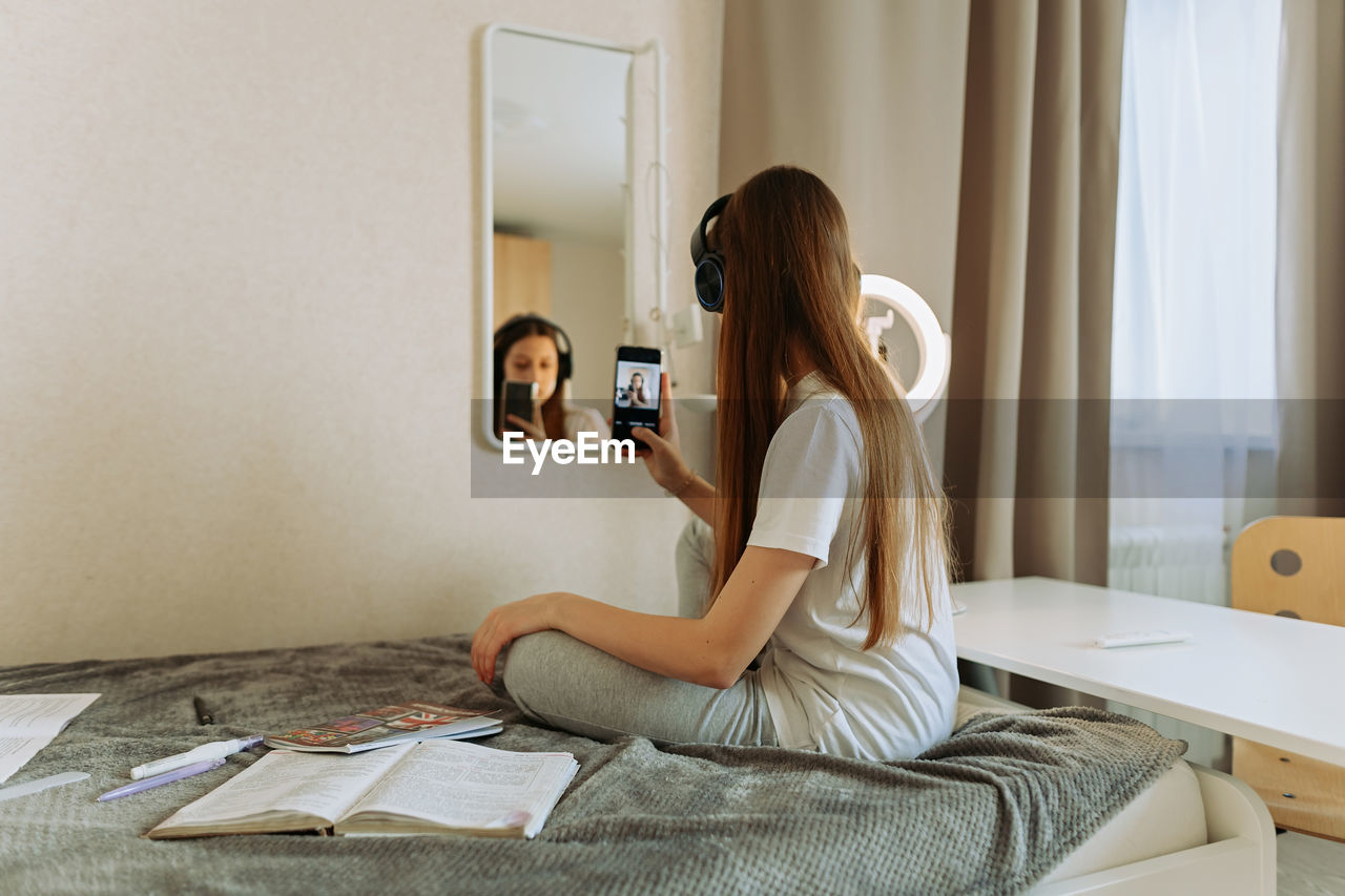 Teenage girl in headphones in front of the mirror takes selfie, admires. reflection