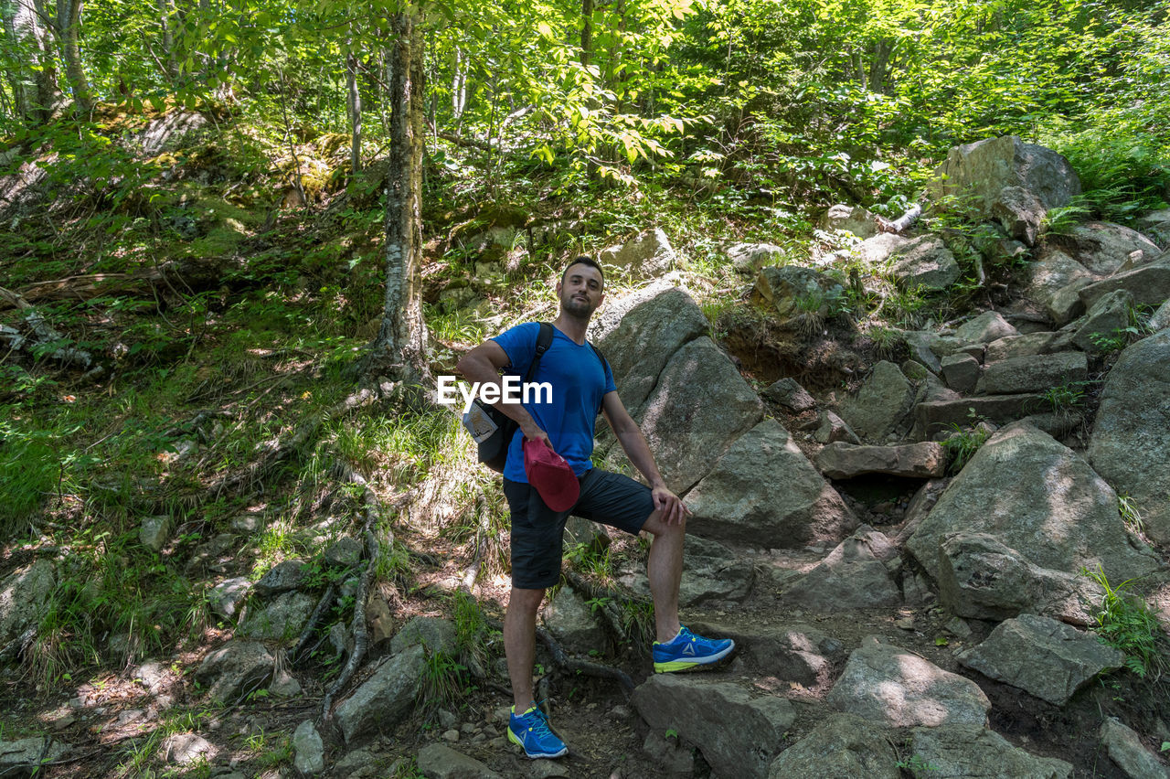 REAR VIEW OF MAN ON ROCK AT FOREST