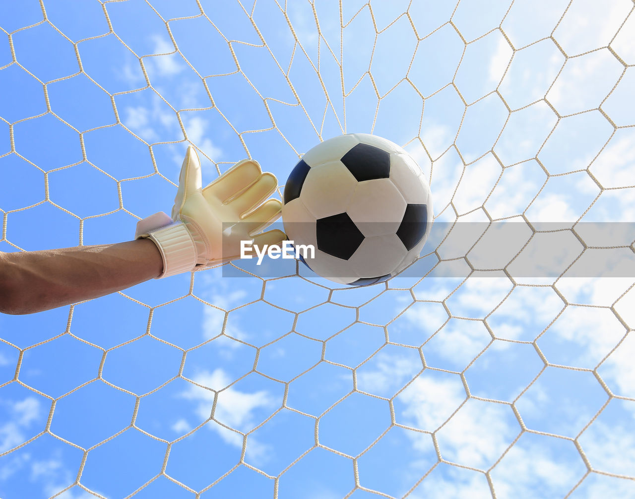 LOW ANGLE VIEW OF HAND PLAYING SOCCER BALL AGAINST BLUE SKY