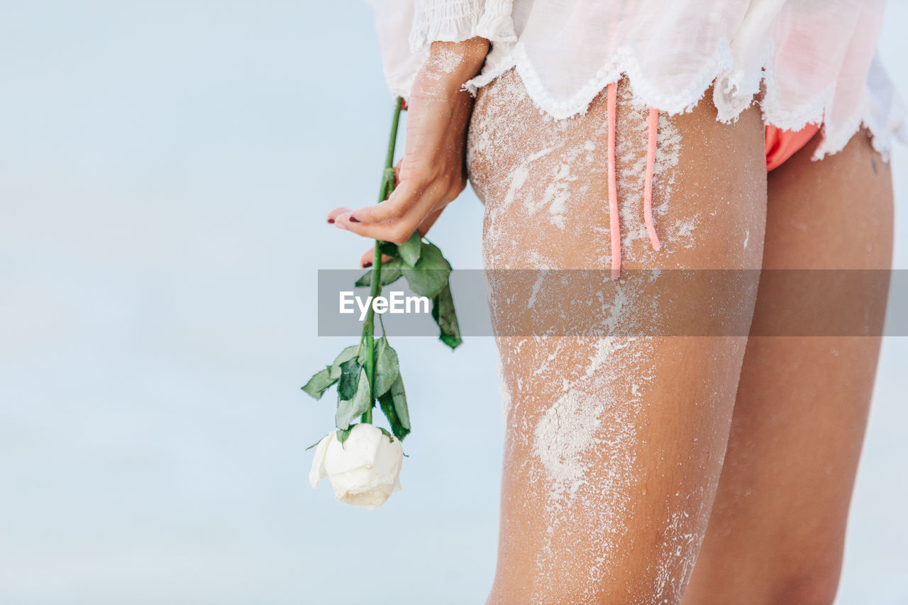 Low section of woman holding rose while standing against sky