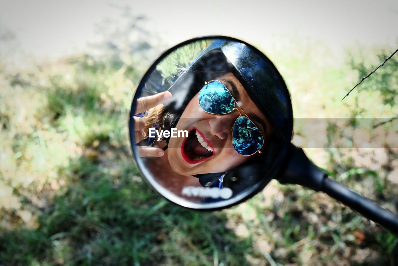 Reflection of woman wearing helmet and sunglasses gesturing horn sign in side-view mirror of motorcycle
