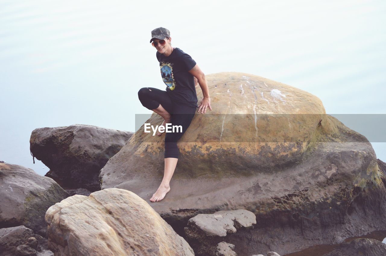 Woman sitting on boulder against sky