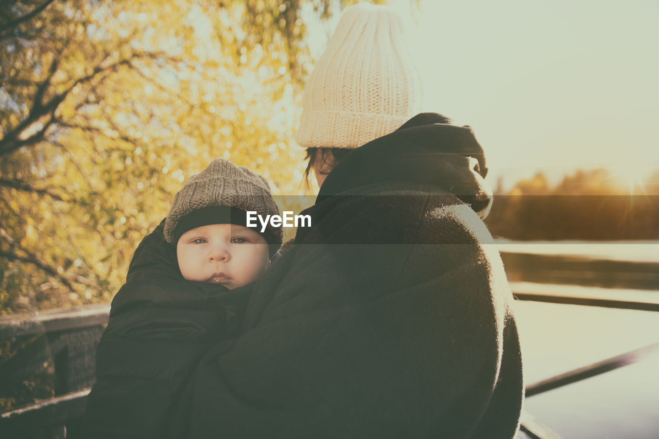 Side view of mother carrying cute son while standing against sky during sunny day