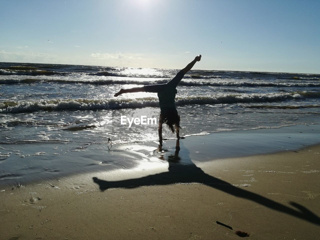 Silhouette woman doing handstand on wet shore