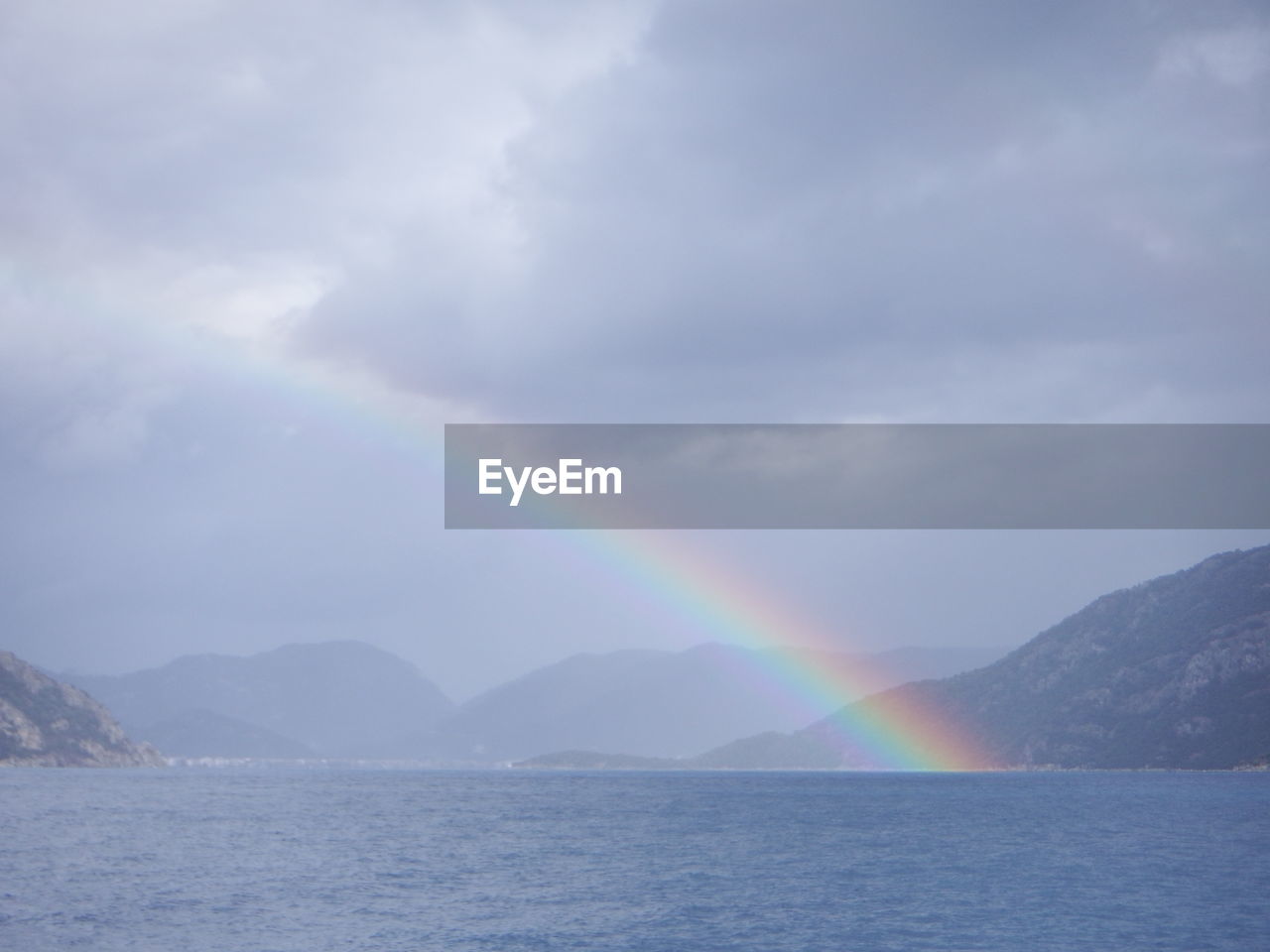 RAINBOW OVER SEA AND MOUNTAINS AGAINST SKY