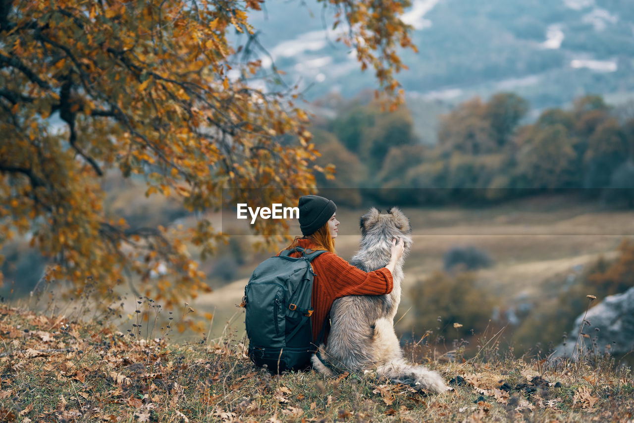 Rear view of woman sitting with dog on field