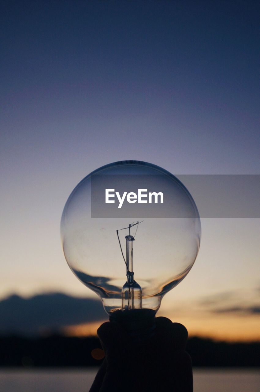 Close-up of illuminated light bulb against sky during sunset