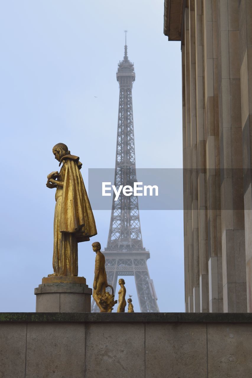 Statues by building against eiffel tower and sky in city 