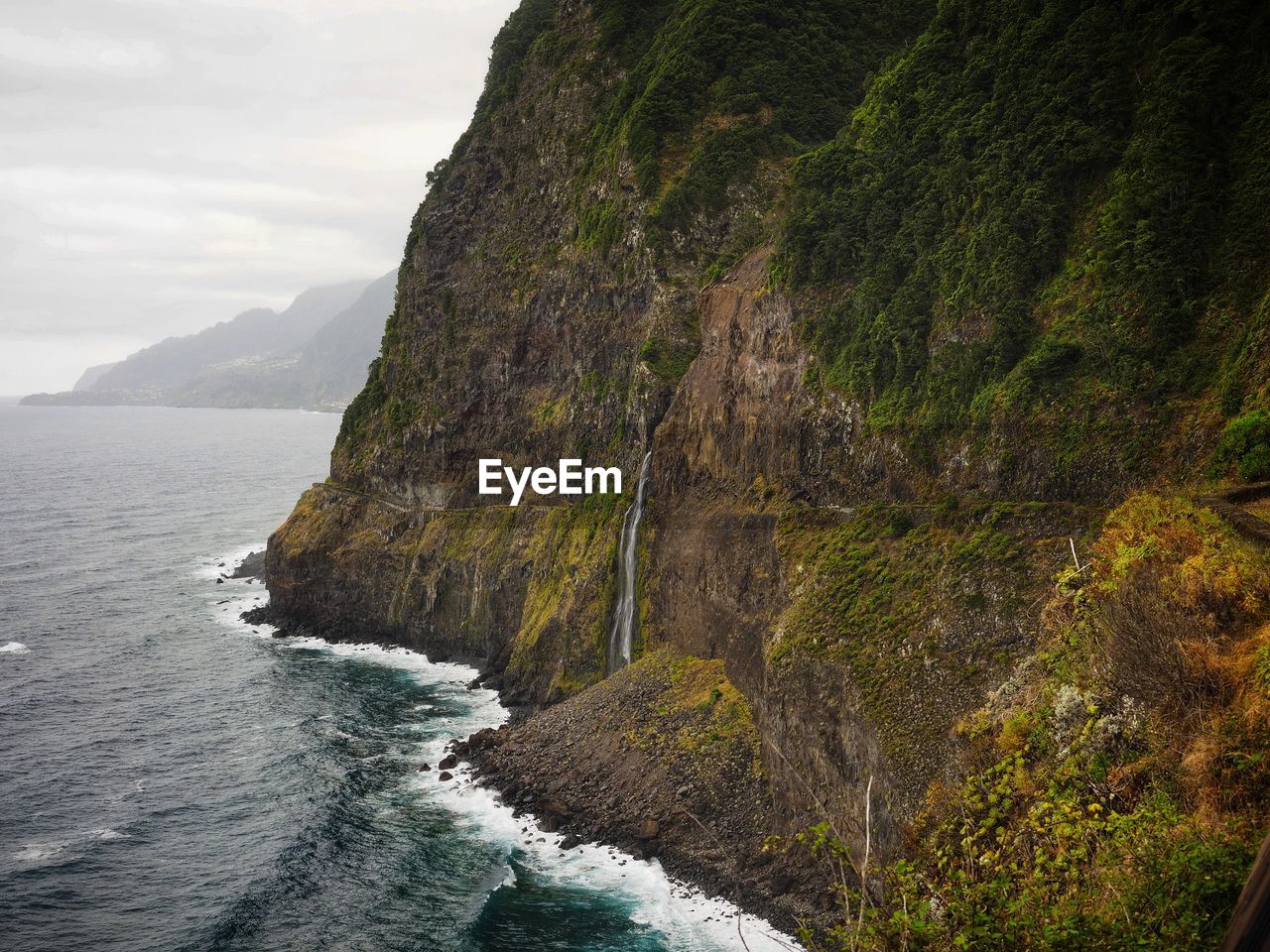 Scenic view of sea by mountain against sky