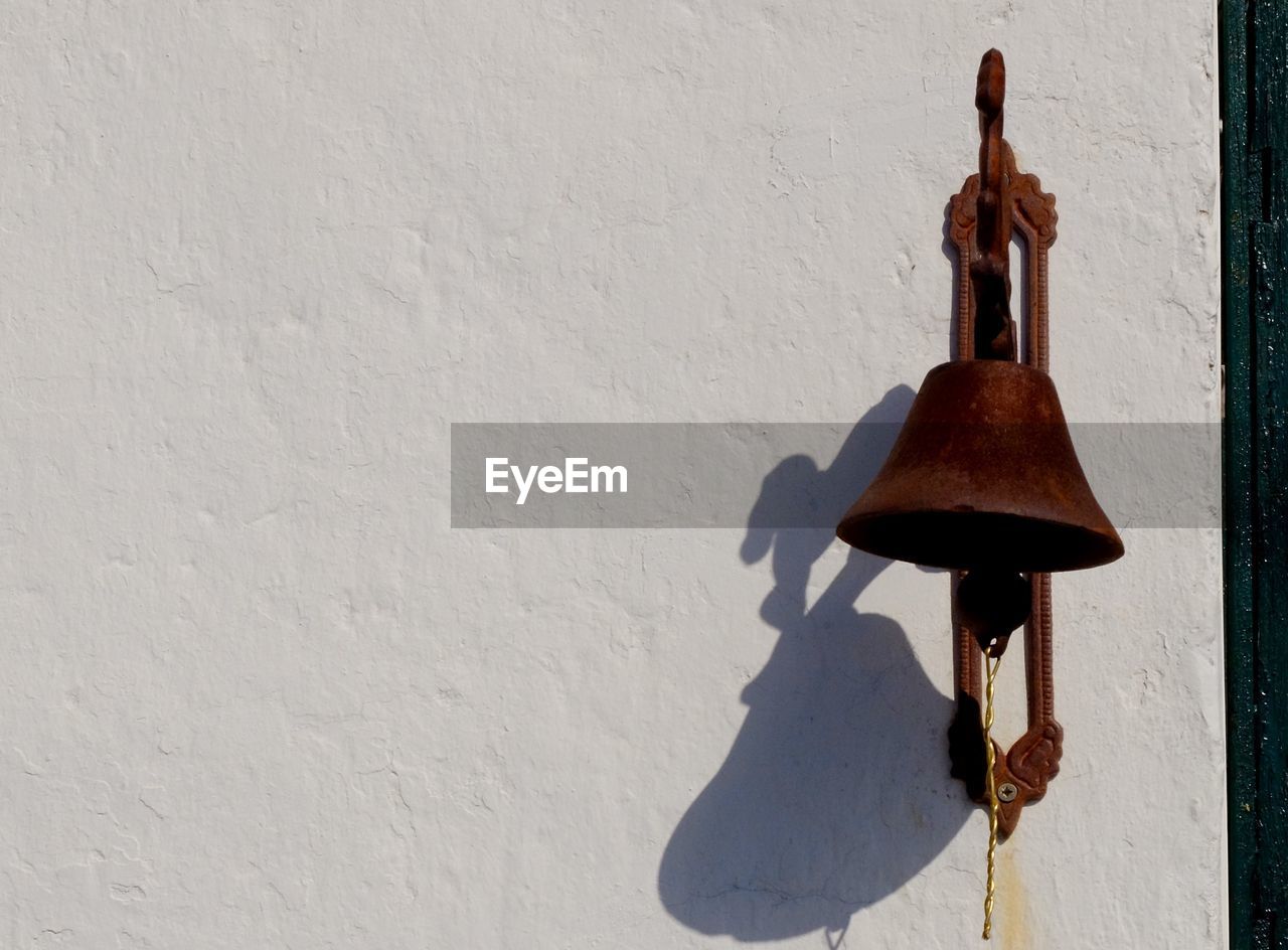 Rusty bell on white wall during sunny day