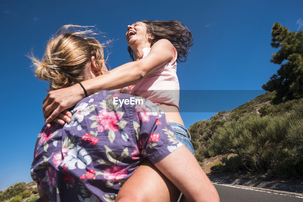 Boyfriend carrying cheerful girlfriend on road during sunny day