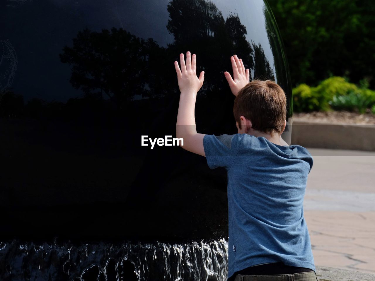 Rear view of boy pushing on built structure at fountain