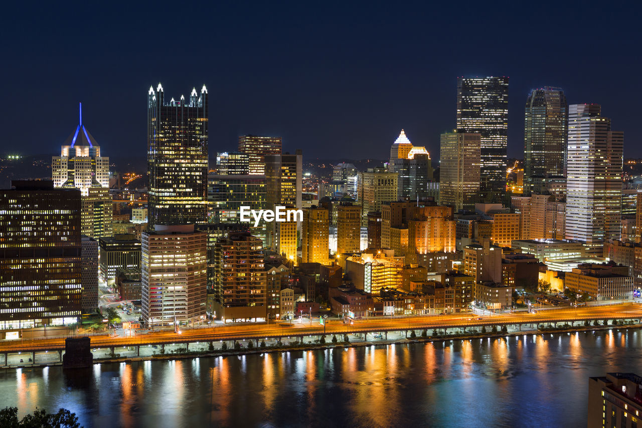 Illuminated buildings by river against sky at night