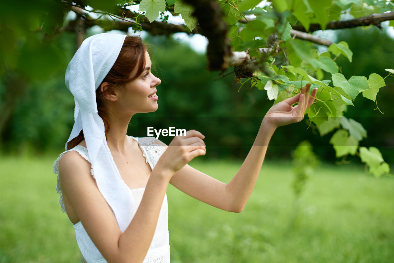 side view of young woman with arms raised standing against plants