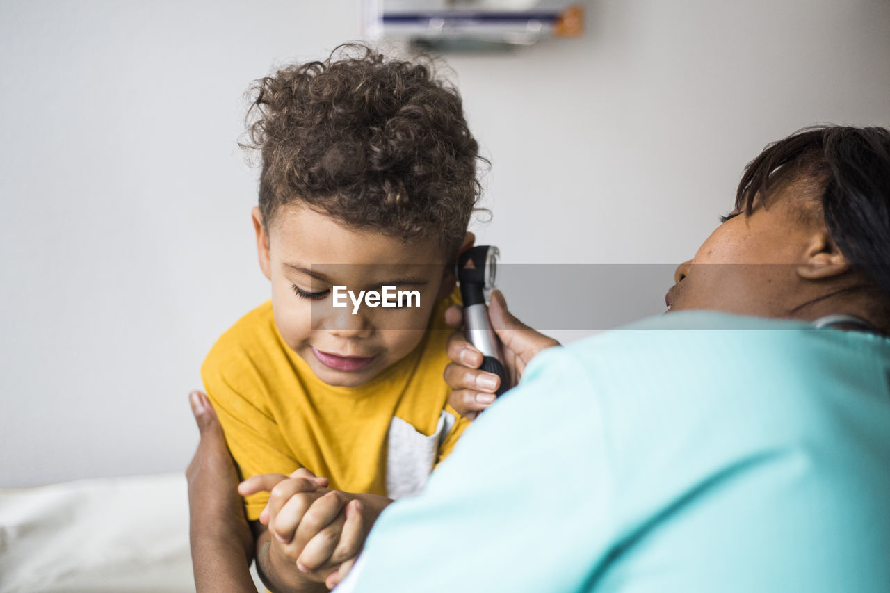 Female pediatrician examining boy's ear in medical clinic