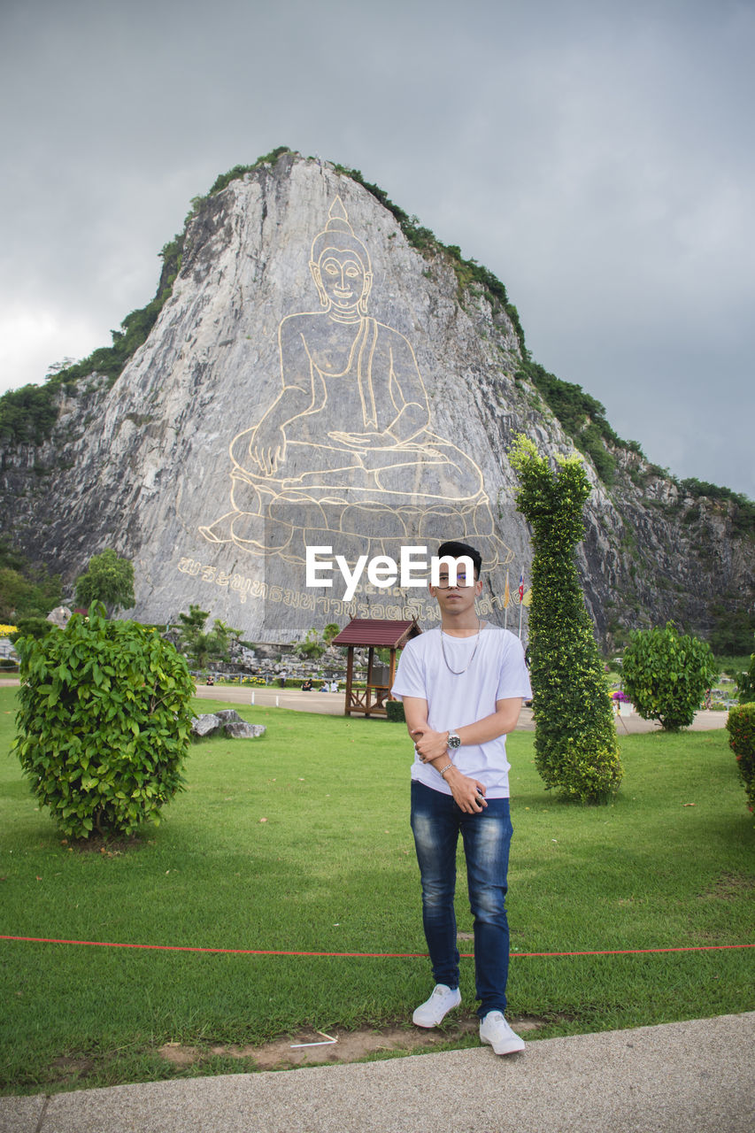 Portrait of young man standing against buddha carving mountain 