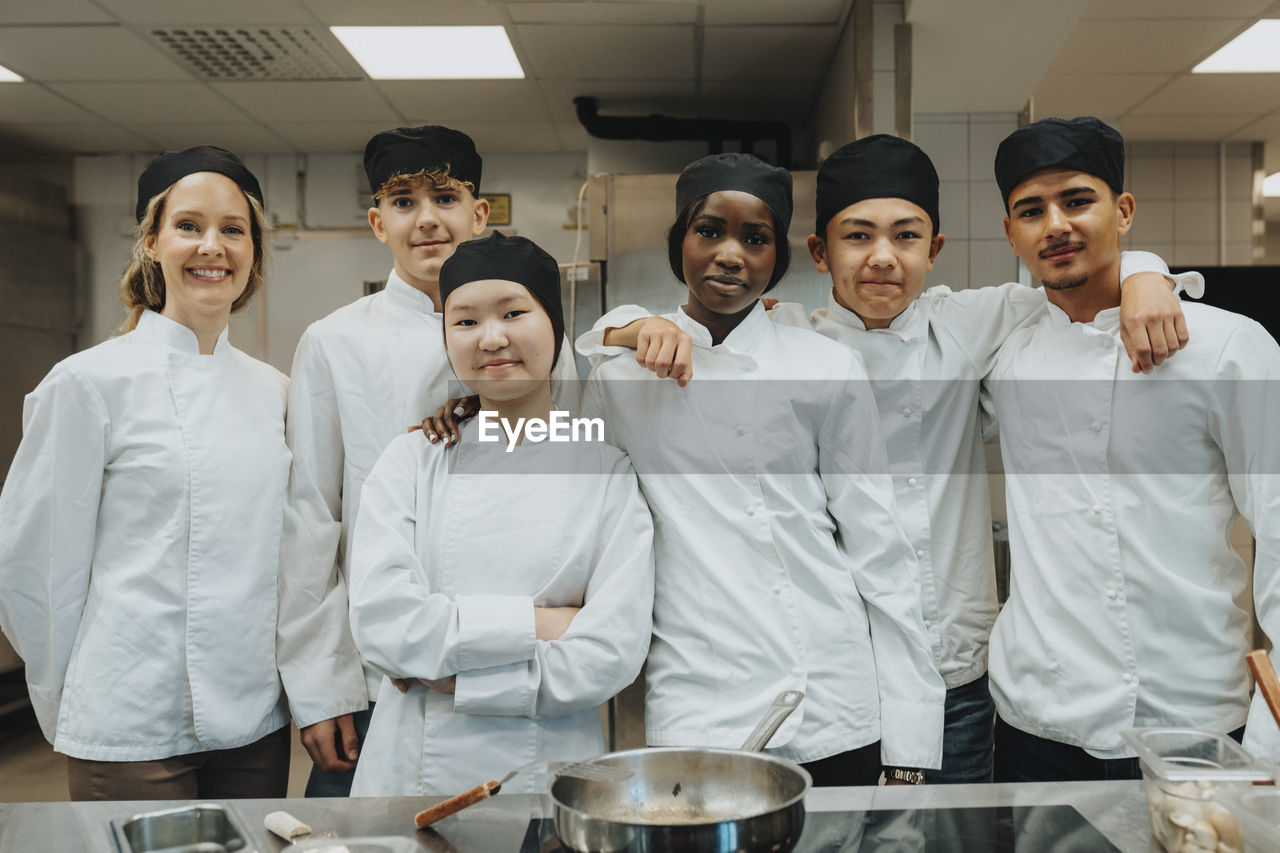 Portrait of male and female trainee standing with teacher in commercial kitchen