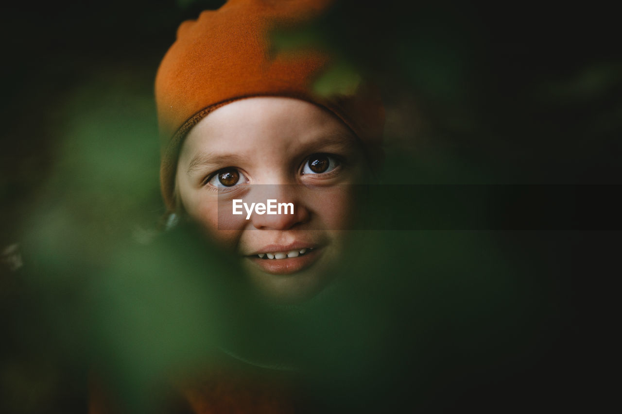 Pretty boy's face between leaves wearing a beanie hat