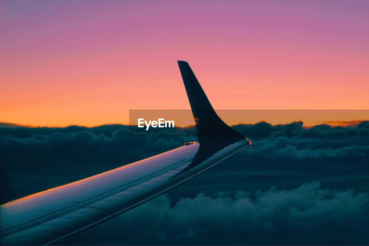 Cropped airplane wing against clear sky during sunset