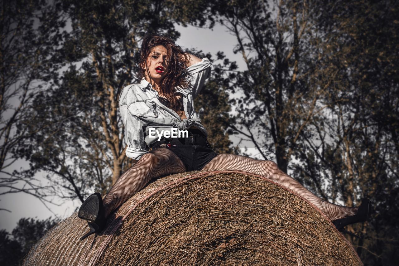 Low angle portrait of seductive woman sitting on hay bale