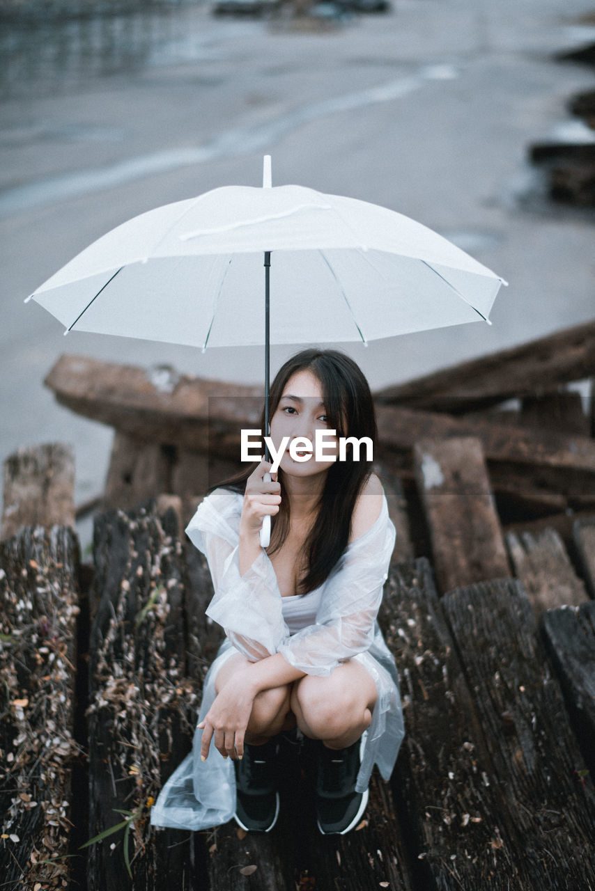 Portrait of young woman with umbrella sitting outdoors